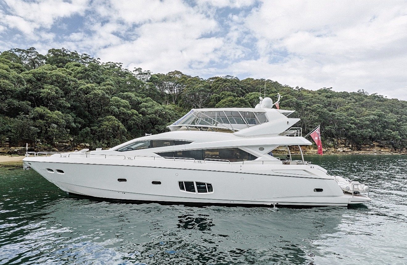 Sunseeker 80 flybridge motor yacht at anchor in a bush-lined bay